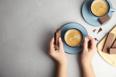 Photo of Woman having breakfast with cup of delicious coffee and wafer at grey table, top view