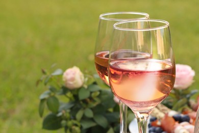 Photo of Glasses of delicious rose wine and food outdoors, closeup