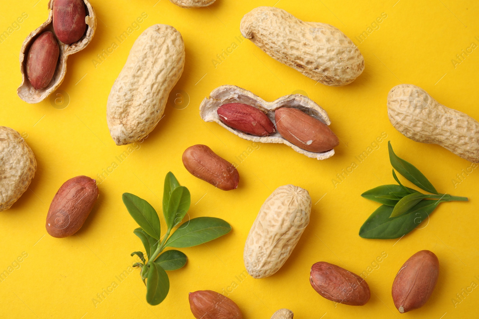 Photo of Fresh peanuts and leaves on yellow table, flat lay