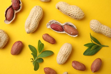 Fresh peanuts and leaves on yellow table, flat lay