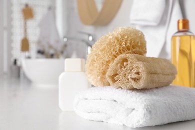 Photo of Natural loofah sponges and towel on table in bathroom. Space for text
