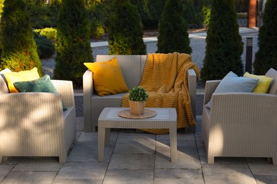 Beautiful rattan garden furniture, soft pillows, blanket and houseplant outdoors