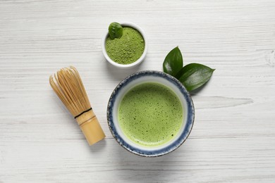 Cup of fresh matcha tea, bamboo whisk and green powder on white wooden table, flat lay