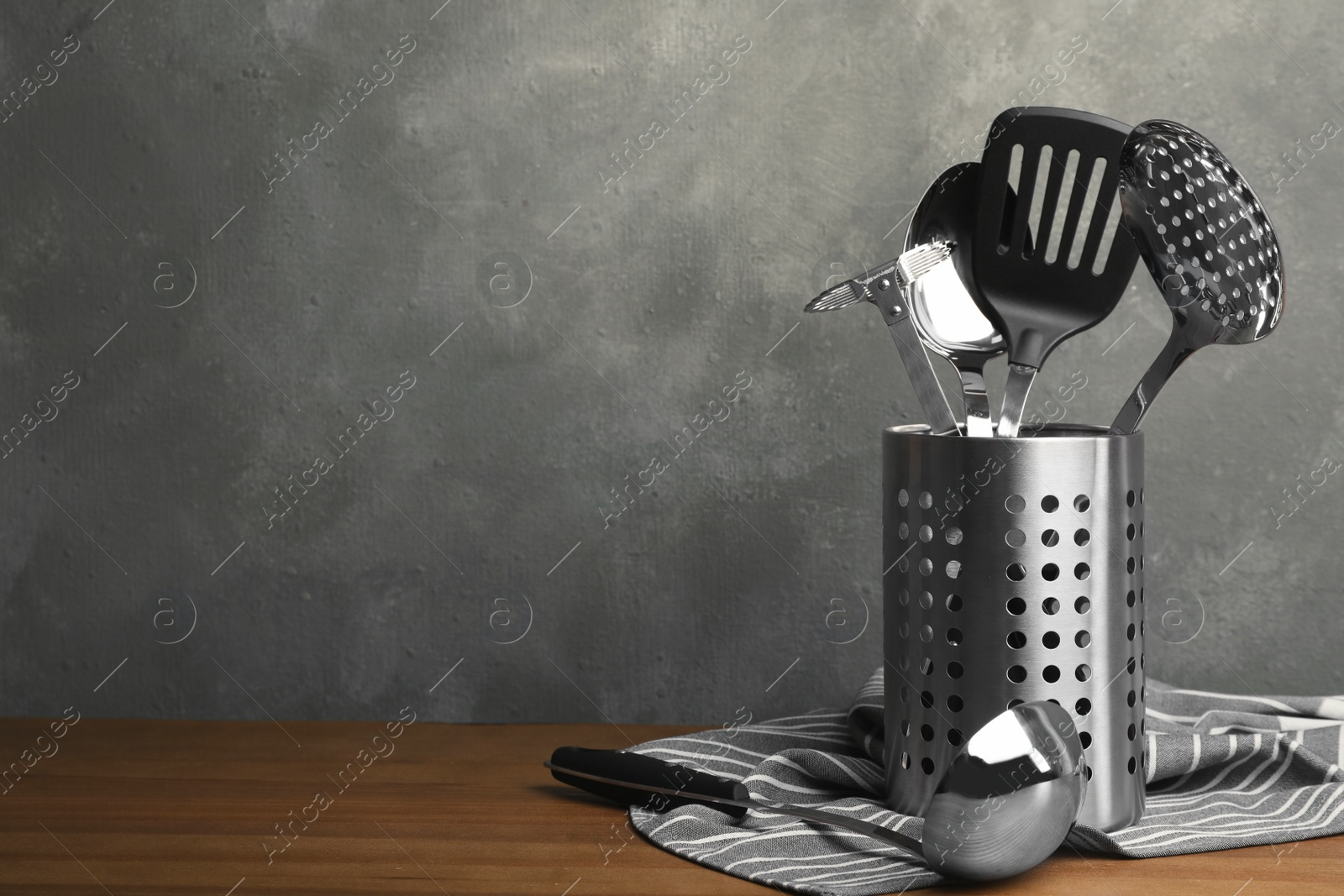 Photo of Holder with clean kitchen utensils and napkin on table. Space for text