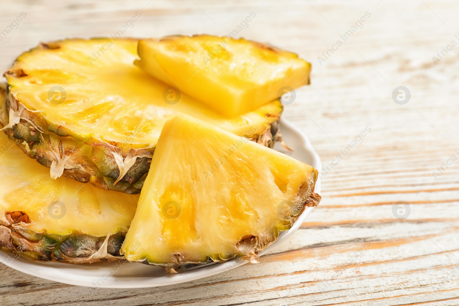 Photo of Plate with fresh pineapple slices on wooden background