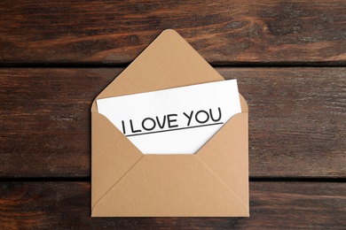 Card with phrase I Love You in envelope on wooden table, top view