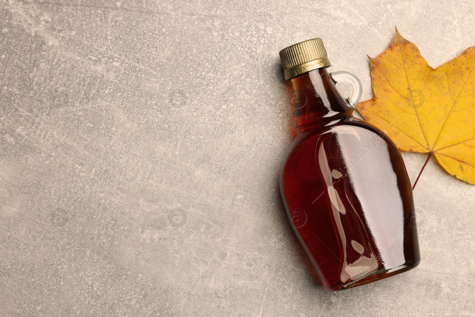 Photo of Bottle of tasty maple syrup and dry leaf on light grey table, flat lay. Space for text