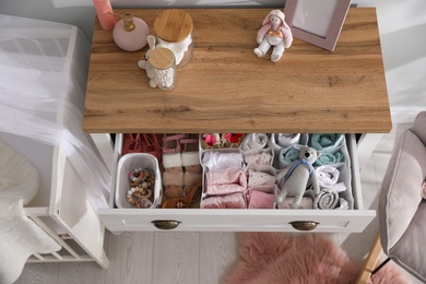 Modern open chest of drawers with baby clothes and accessories in room, above view