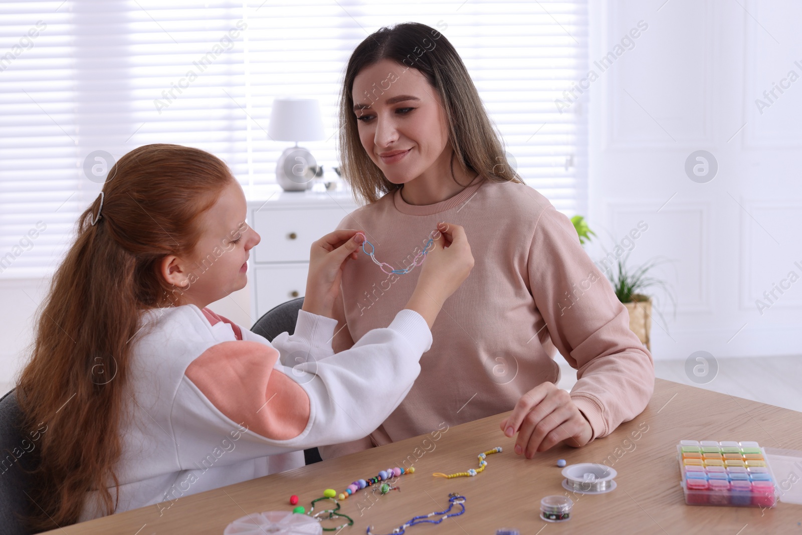 Photo of Happy mother with her daughter making beaded jewelry at home