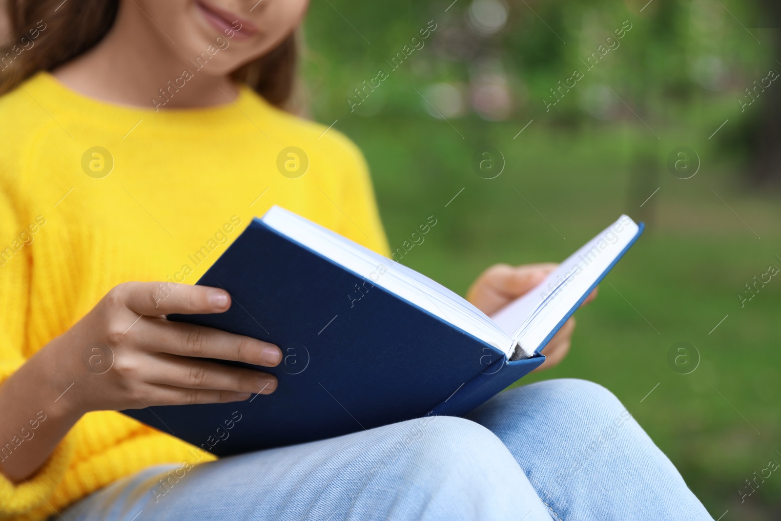 Photo of Cute little girl reading book in green park, closeup