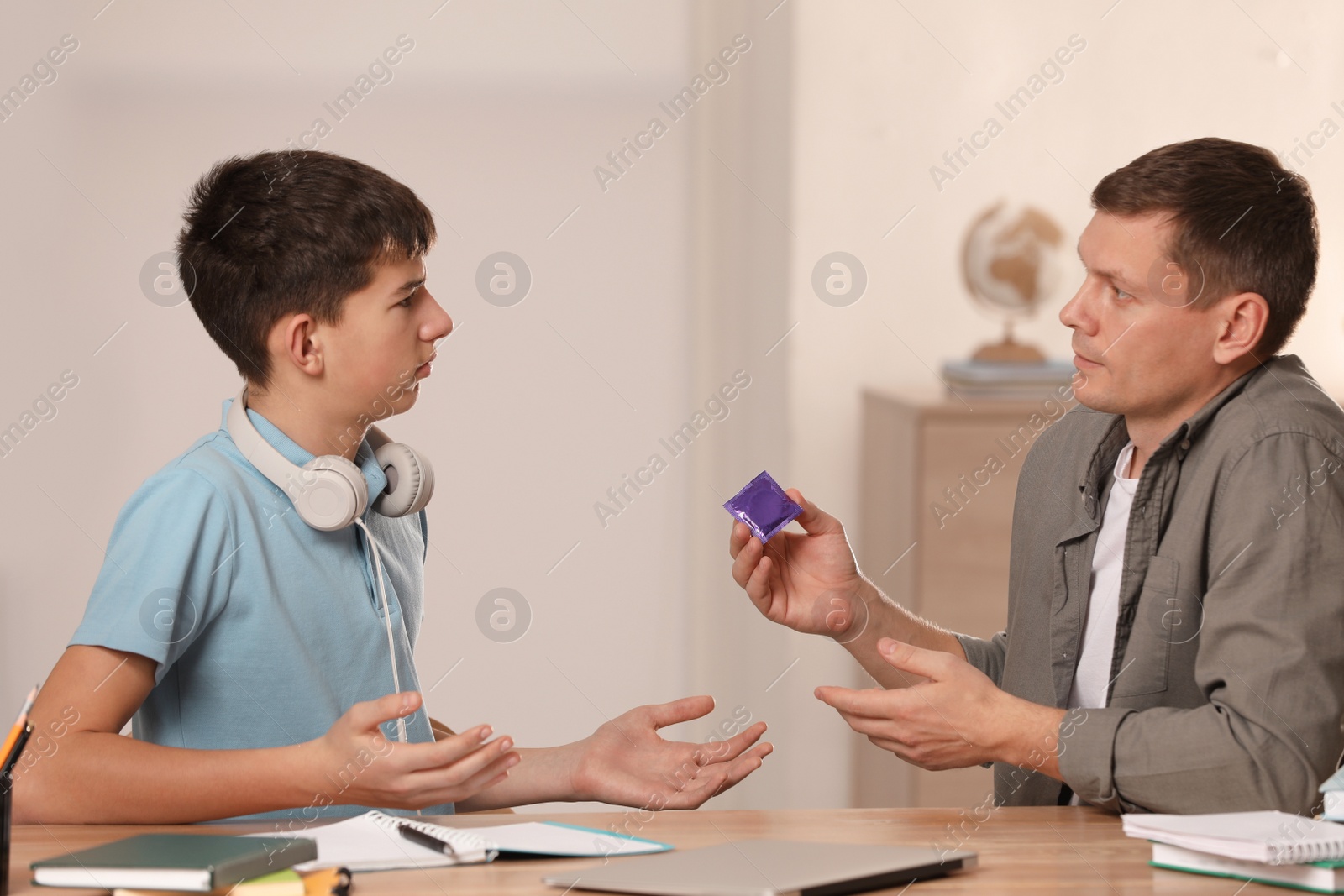 Photo of Father talking with his teenage son about contraception while he doing homework at home. Sex education concept