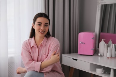 Photo of Woman near dressing table with cosmetic fridge indoors