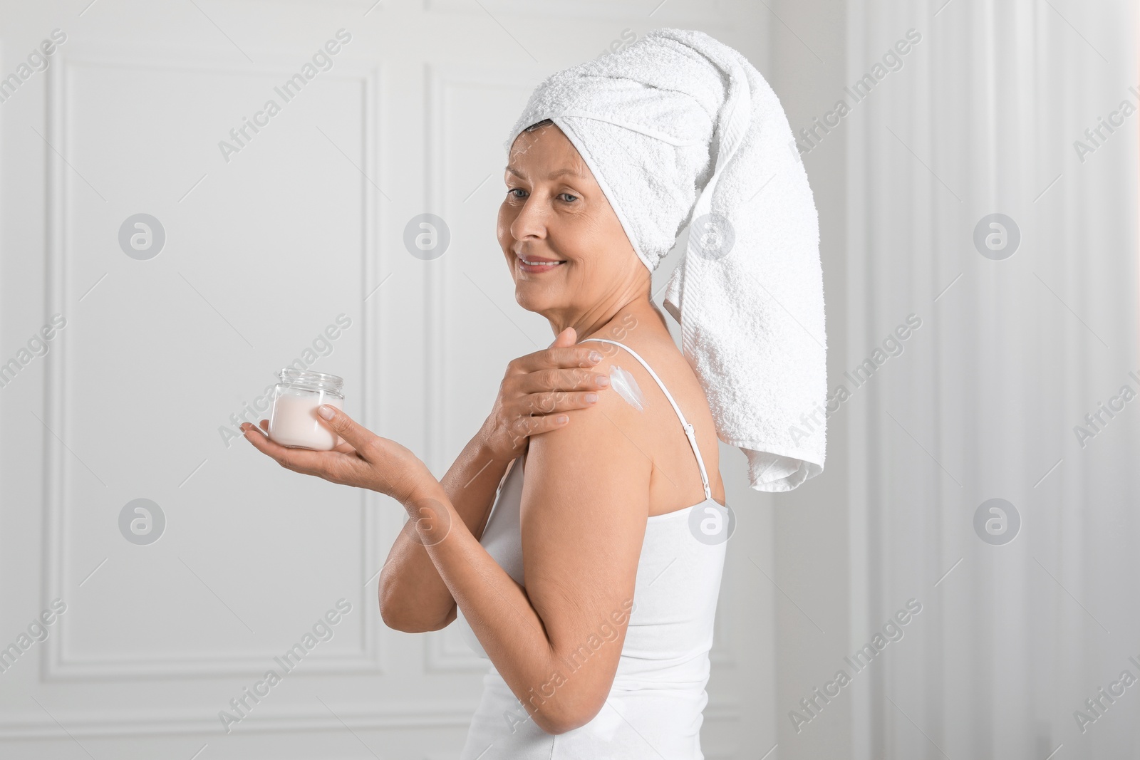 Photo of Happy woman applying body cream onto shoulder near white wall