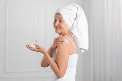 Photo of Happy woman applying body cream onto shoulder near white wall