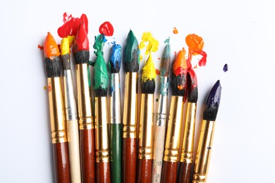 Brushes with colorful paints on white background, flat lay