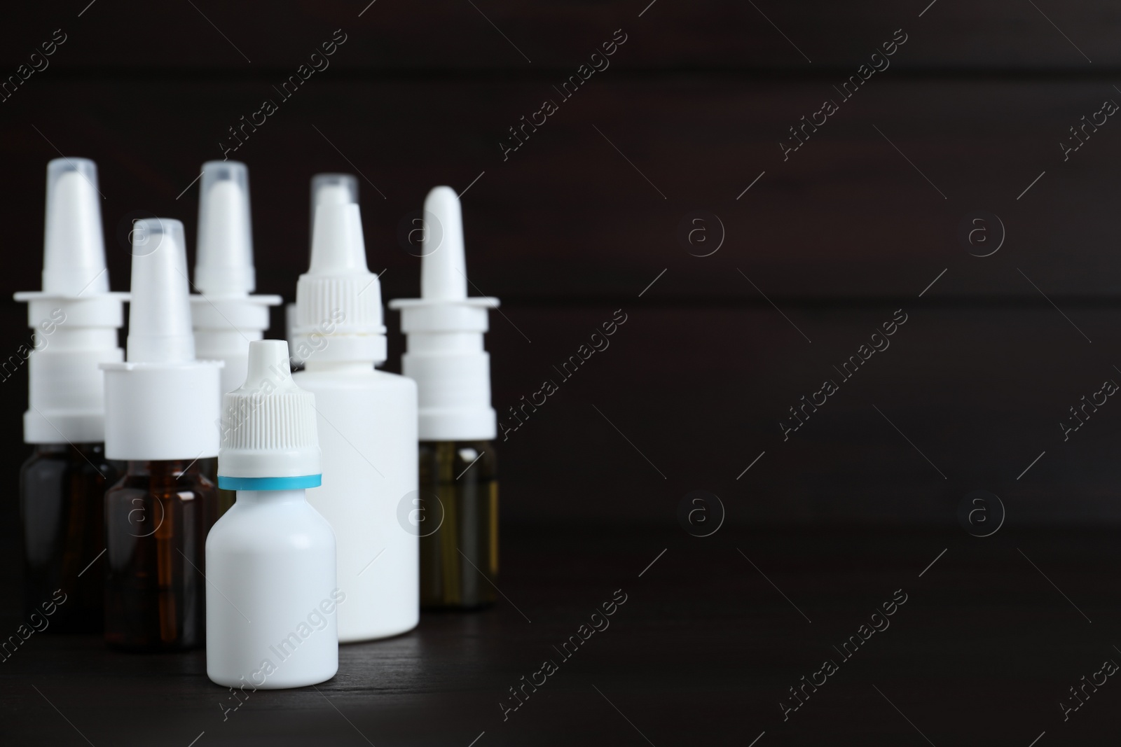Photo of Bottles of nasal sprays on black wooden table. Space for text