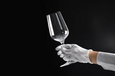 Person in white glove checking cleanliness of glass on dark background, closeup. Space for text