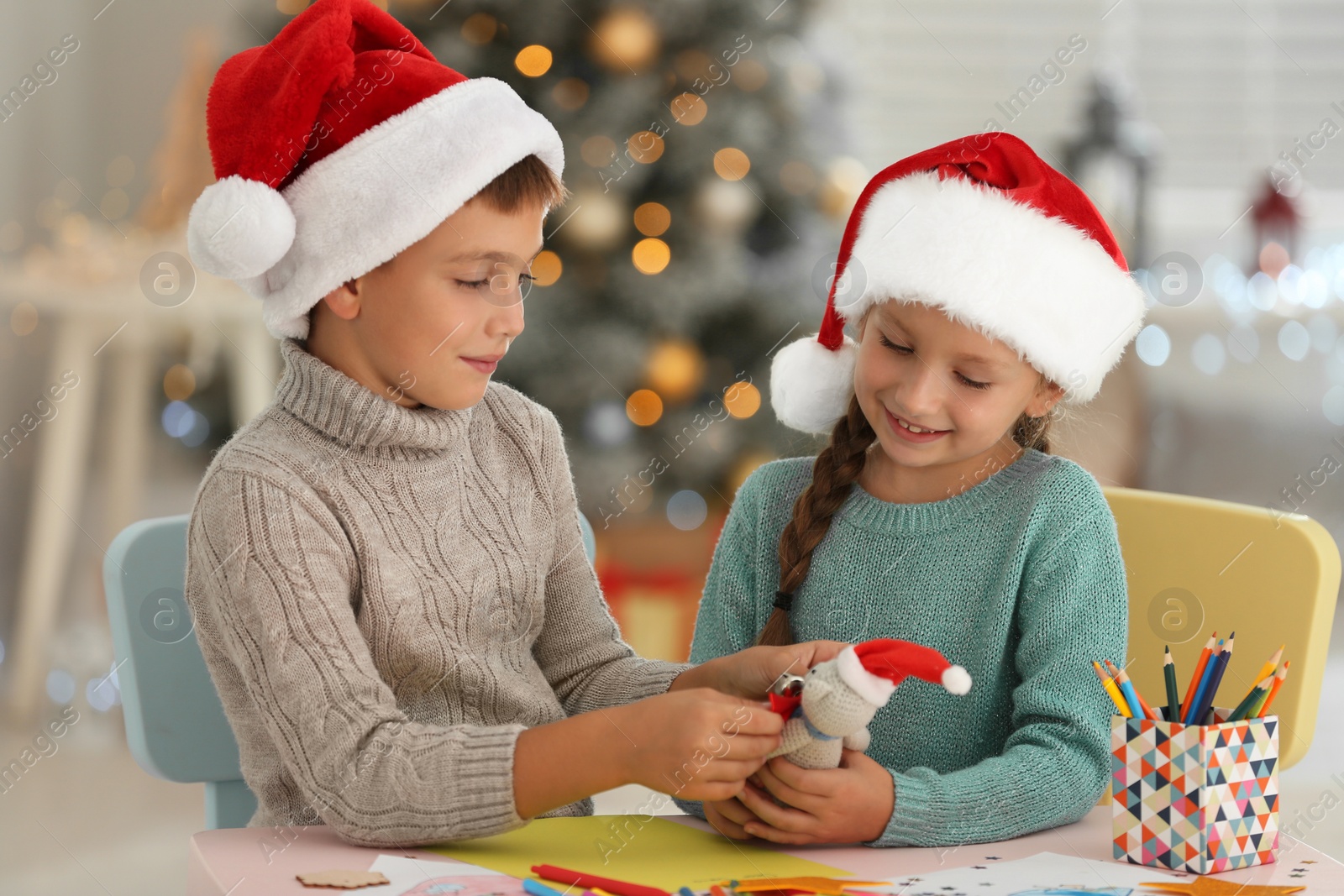 Photo of Little children in Santa hats making toy at table indoors. Christmas season