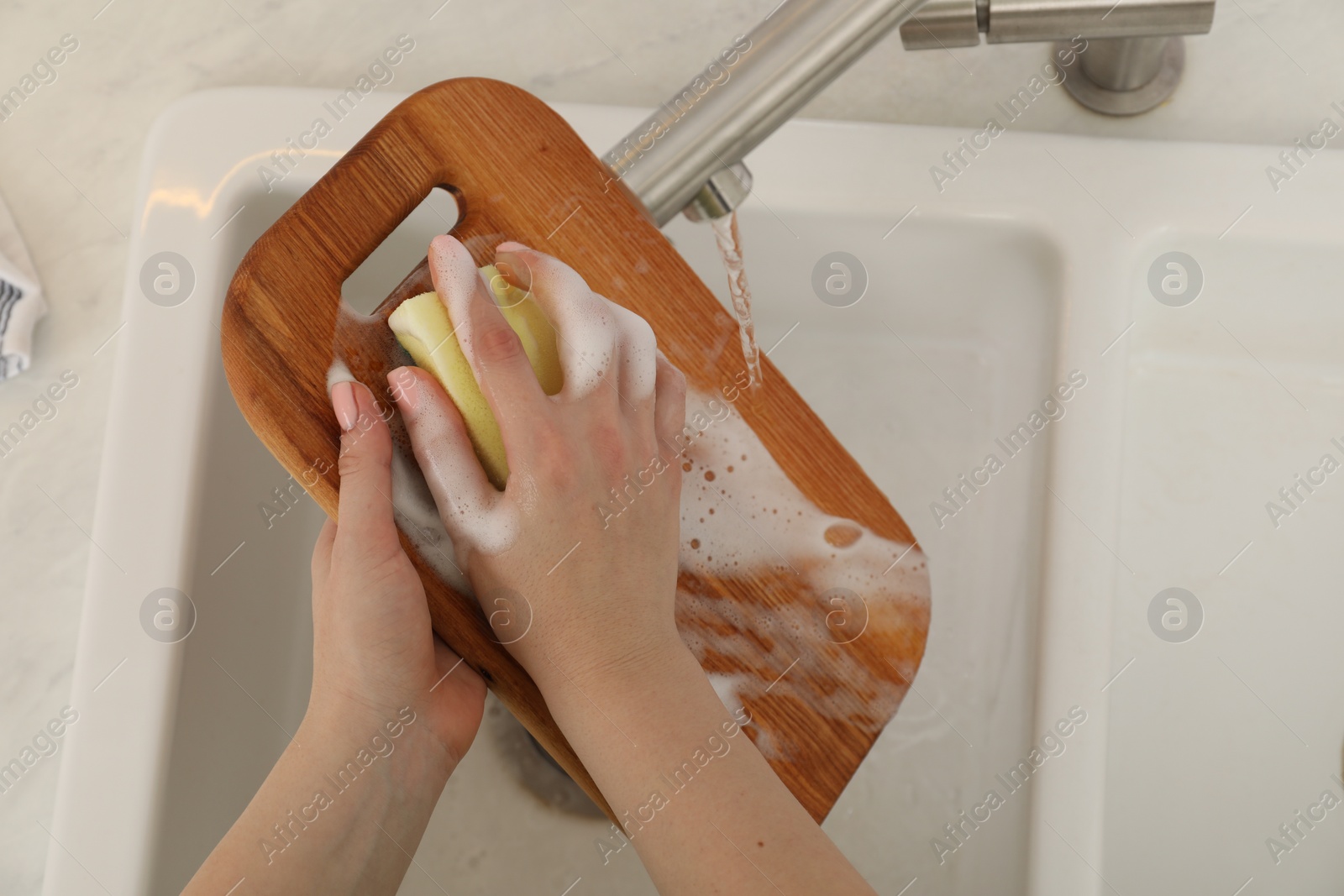 Photo of Woman washing wooden cutting board at sink in kitchen, top view