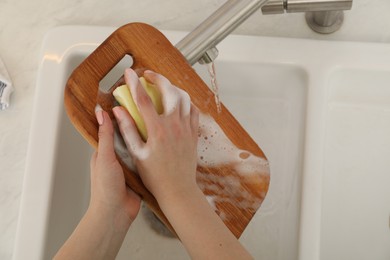 Woman washing wooden cutting board at sink in kitchen, top view