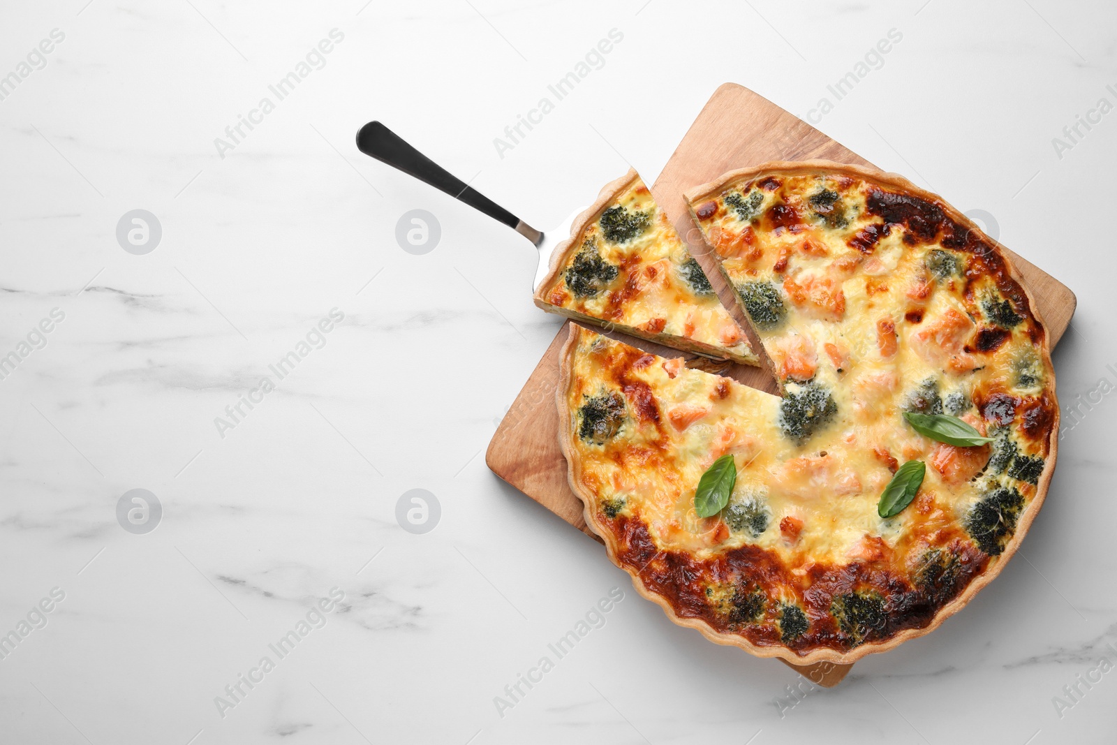 Photo of Delicious homemade salmon quiche with broccoli and spatula on white marble table, top view. Space for text
