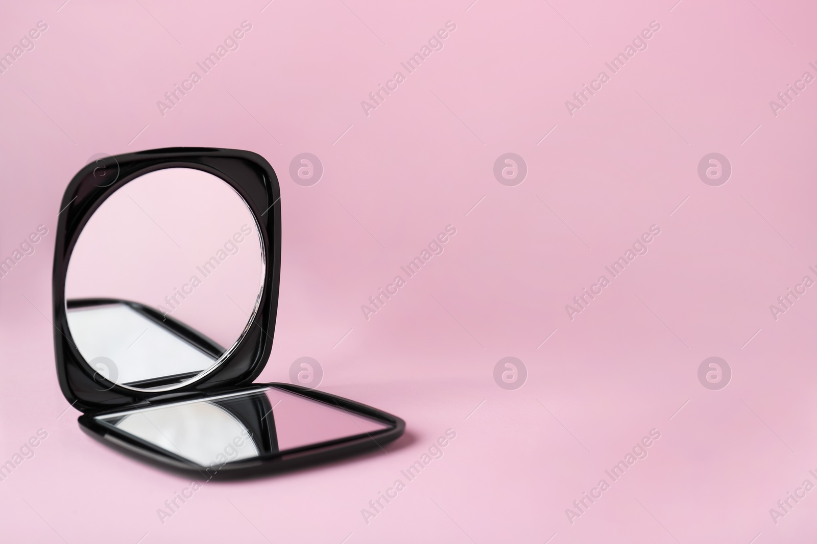 Photo of Stylish cosmetic pocket mirror on pink background. Space for text