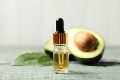 Bottle of essential oil and avocado on light blue wooden table