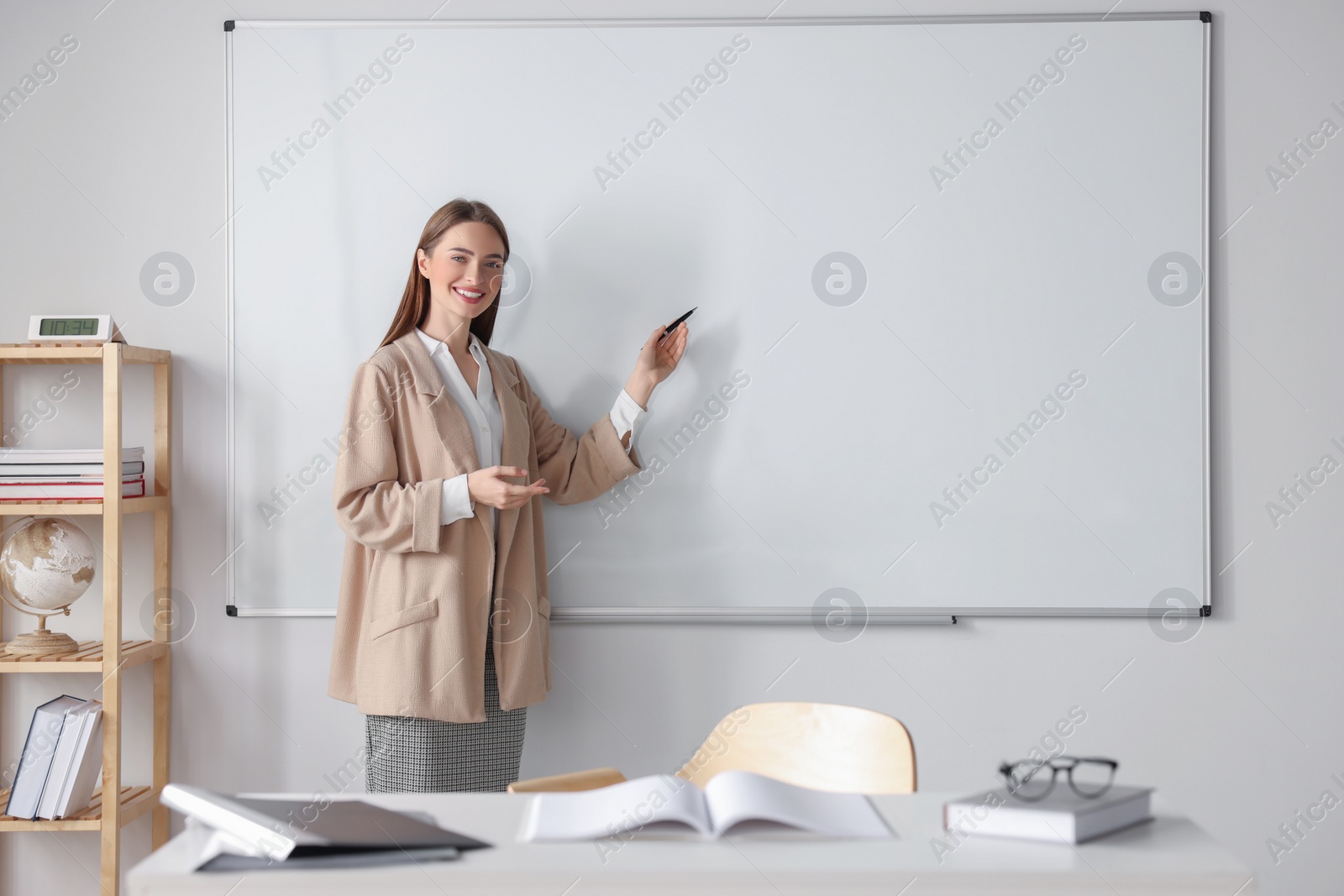 Photo of Happy young teacher explaining something at whiteboard in classroom. Space for text