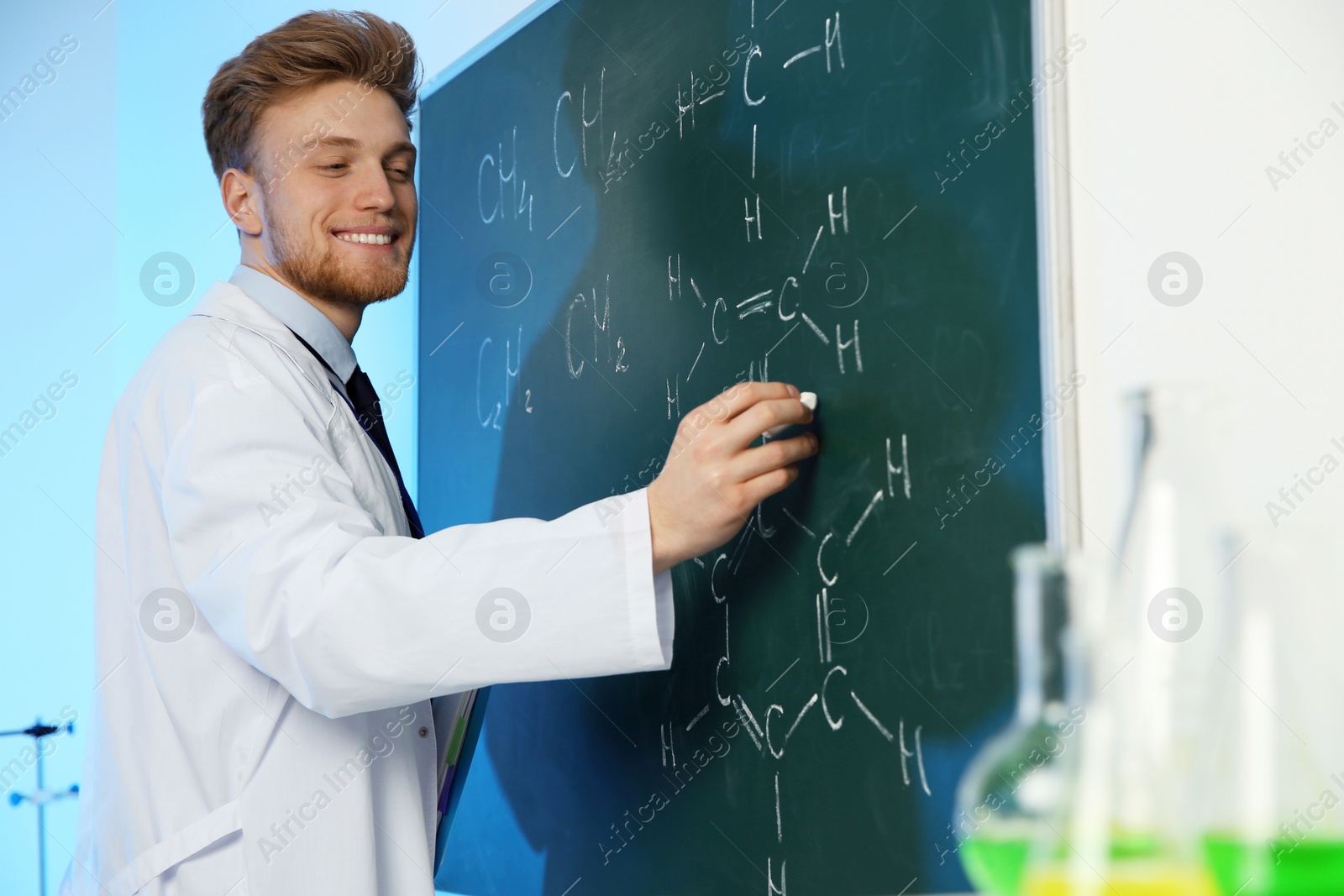 Photo of Male scientist writing chemical formula on chalkboard indoors