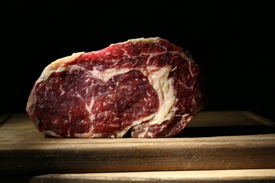 Photo of Piece of raw beef meat on wooden board against black background, closeup