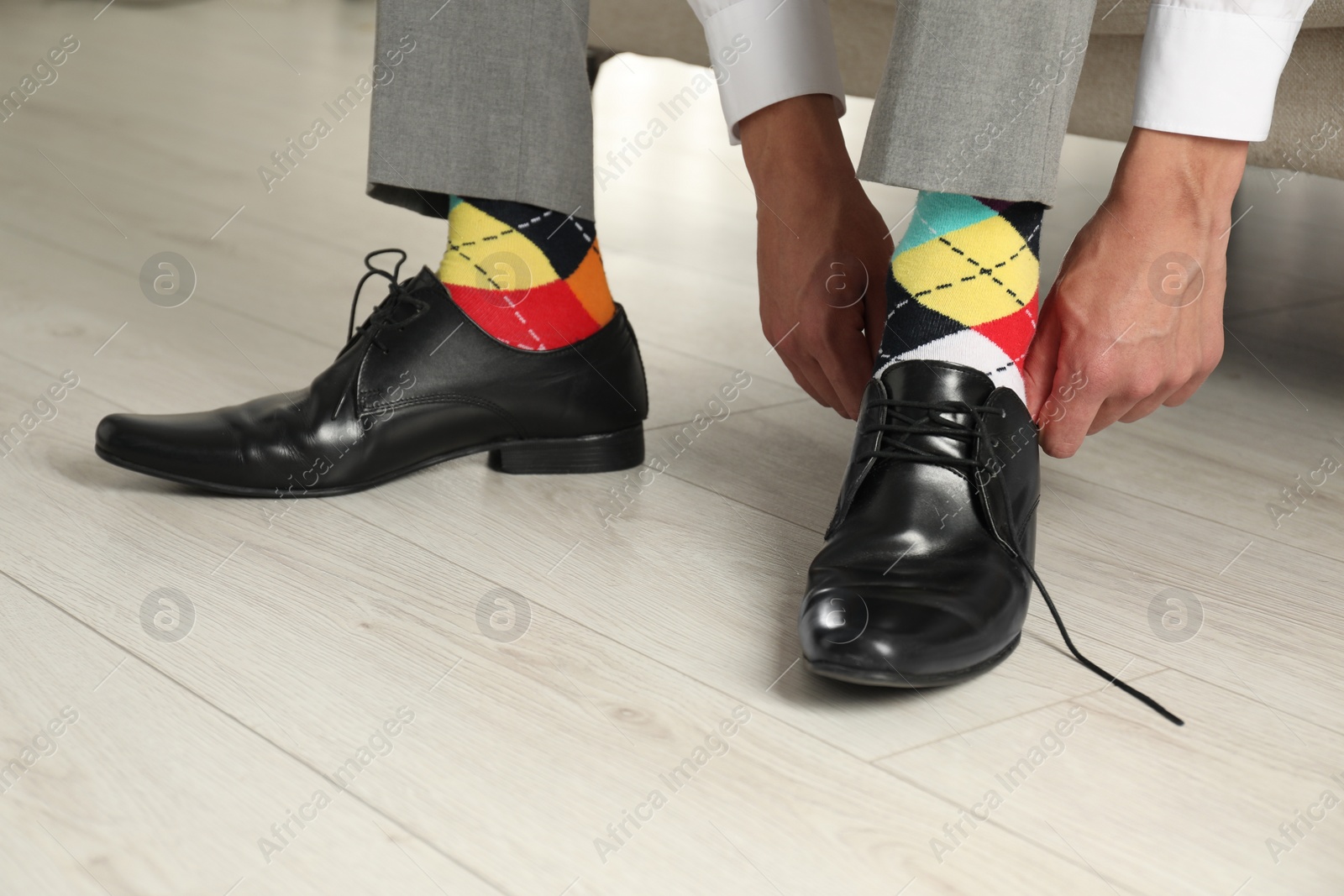 Photo of Man with colorful socks putting on stylish shoes indoors, closeup