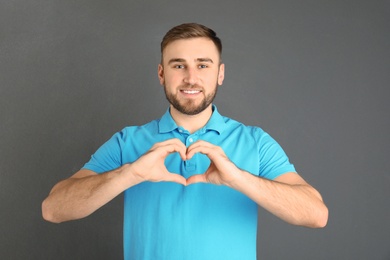 Young man making heart with his hands on grey background