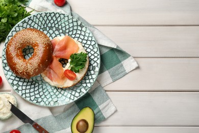 Delicious bagel with cream cheese, jamon, tomato and parsley on white wooden table, flat lay. Space for text