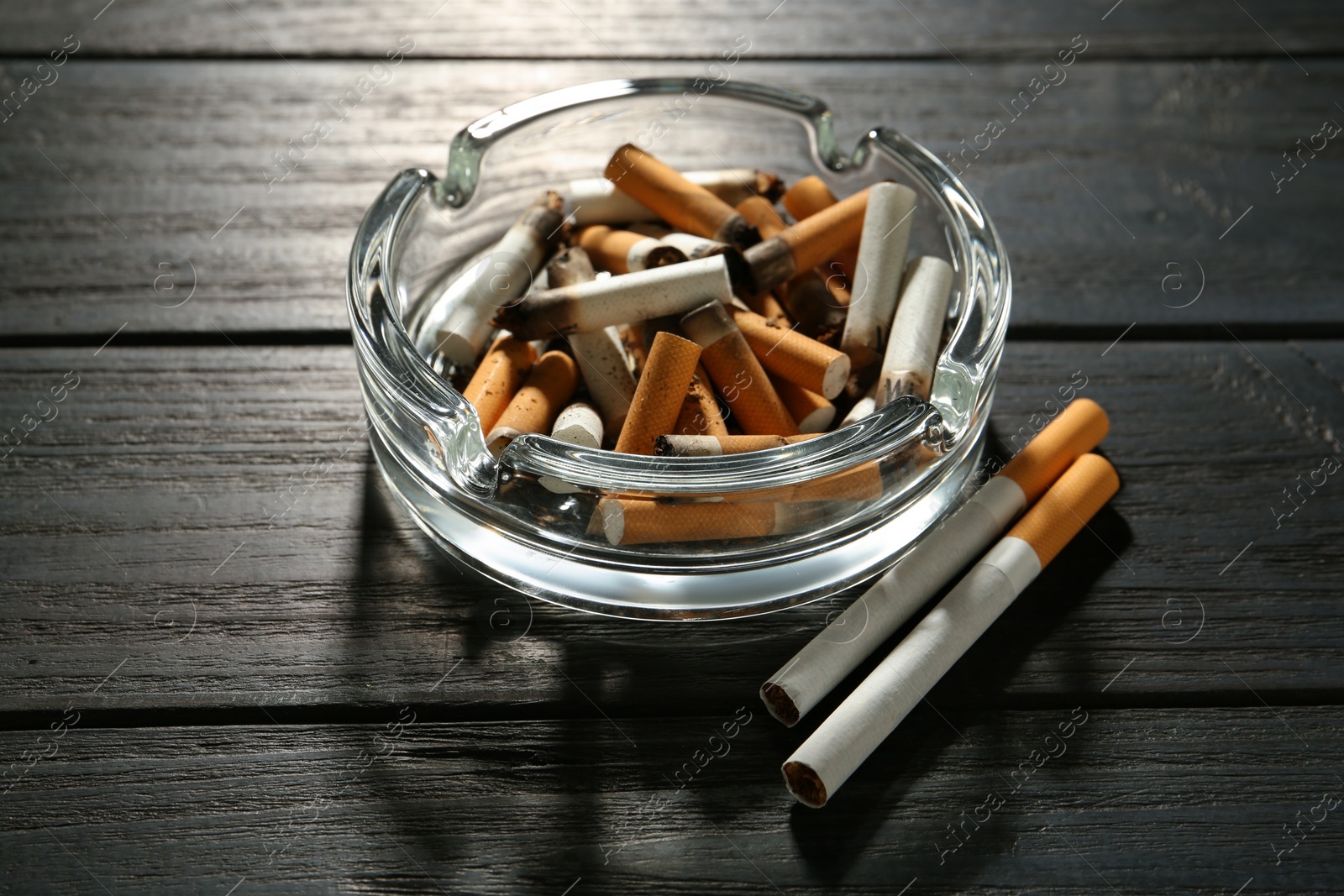 Photo of Glass ashtray with cigarette stubs on black wooden table