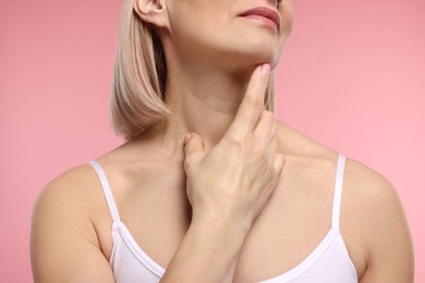 Photo of Woman touching her neck on pink background, closeup