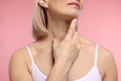 Woman touching her neck on pink background, closeup