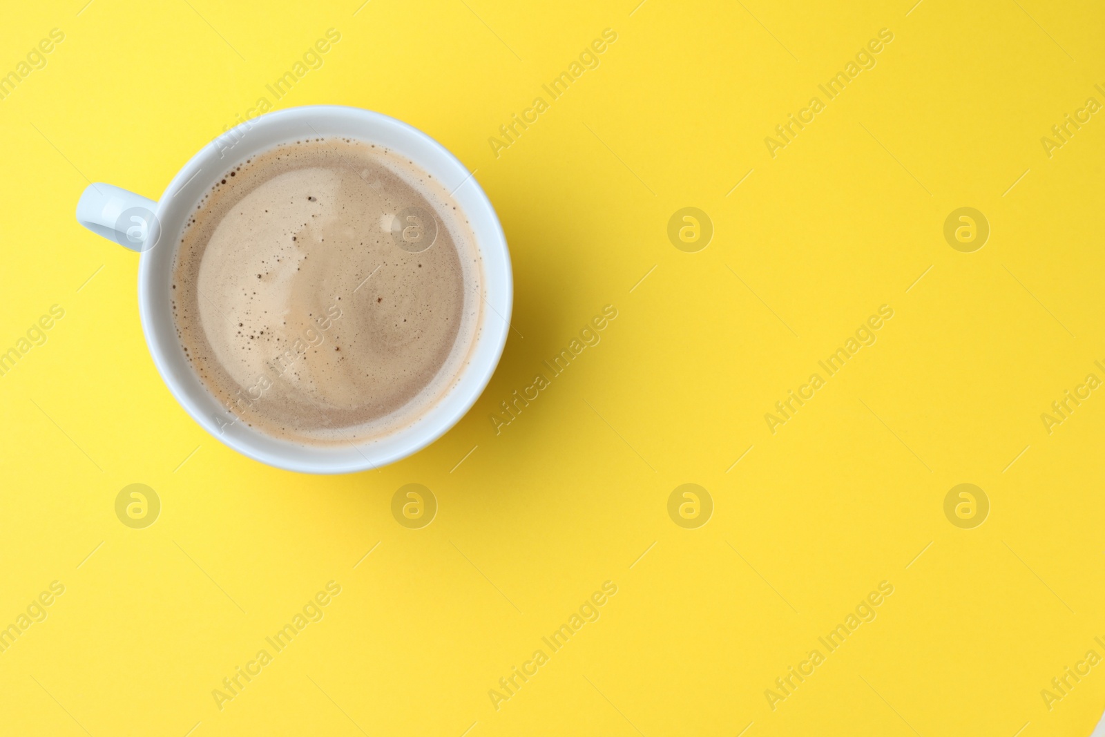 Photo of White mug of freshly brewed hot coffee on yellow background, top view. Space for text