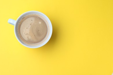 Photo of White mug of freshly brewed hot coffee on yellow background, top view. Space for text
