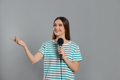 Young female journalist with microphone on grey background