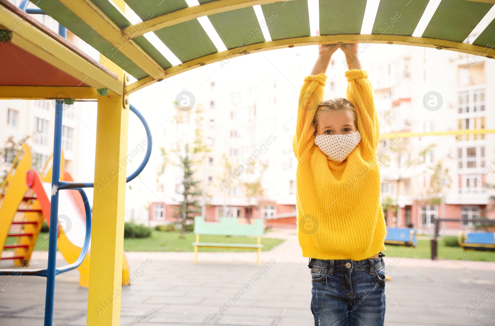 Photo of Little girl with medical face mask on playground during covid-19 quarantine