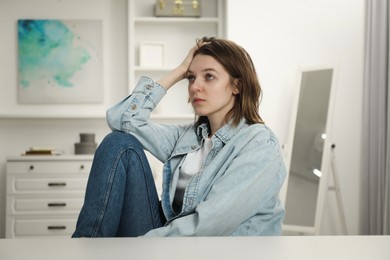 Photo of Sad young woman sitting at white table in room