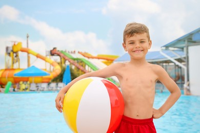 Photo of Cute little boy with inflatable ball near pool in water park, space for text