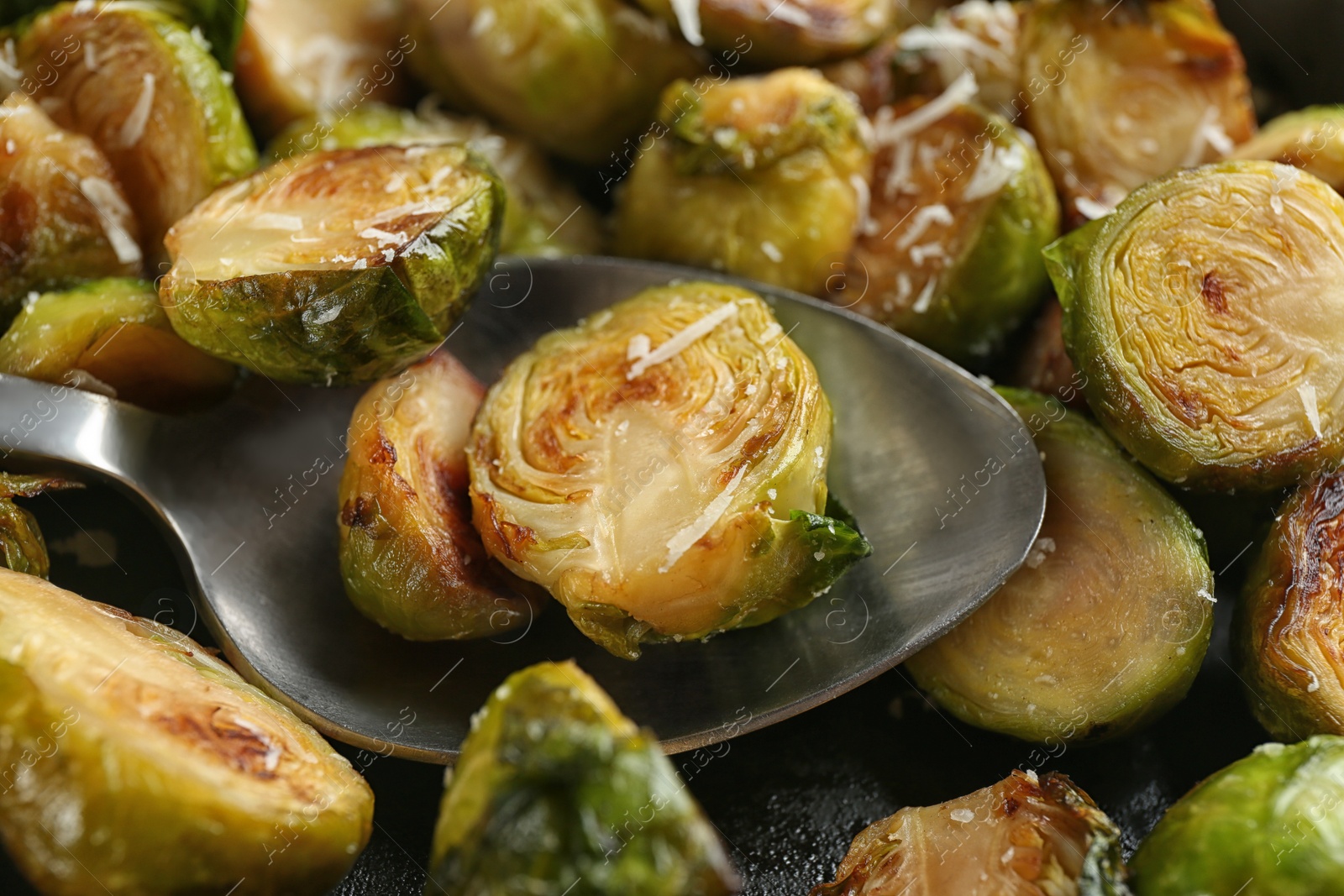 Photo of Delicious roasted brussels sprouts with grated cheese and spoon as background, closeup