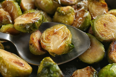 Photo of Delicious roasted brussels sprouts with grated cheese and spoon as background, closeup