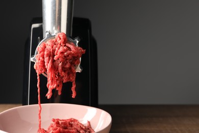 Photo of Electric meat grinder with beef mince on wooden table against grey background, closeup. Space for text
