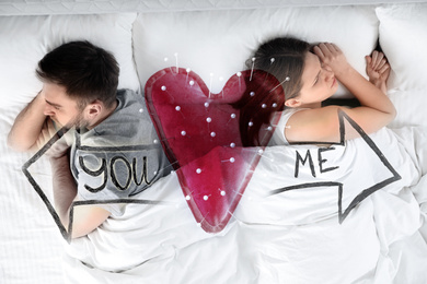 Image of Double exposure of unhappy couple in bed and heart shaped cushion with sewing pins. Relationship problems