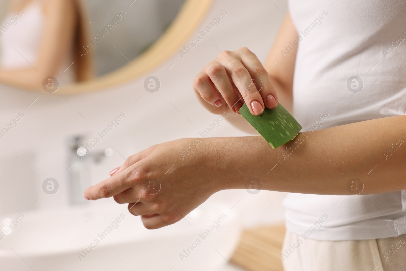 Photo of Young woman applying aloe gel from leaf onto her arm in bathroom, closeup