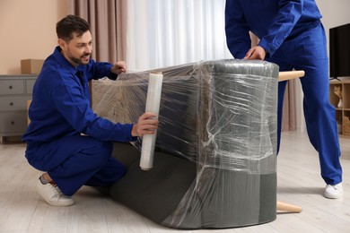 Male movers with stretch film wrapping sofa in new house