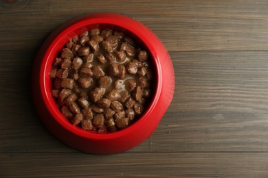 Photo of Wet pet food in feeding bowl on wooden background, top view. Space for text