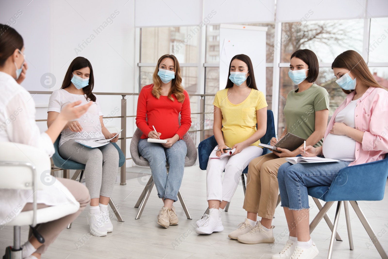 Photo of Group of pregnant women and midwife in protective masks at courses for expectant mothers indoors